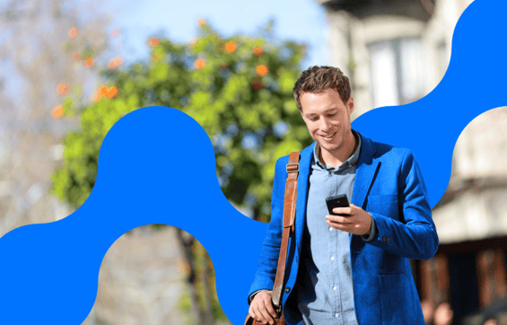 Man in a blue jacket walking outdoors while looking at his smartphone