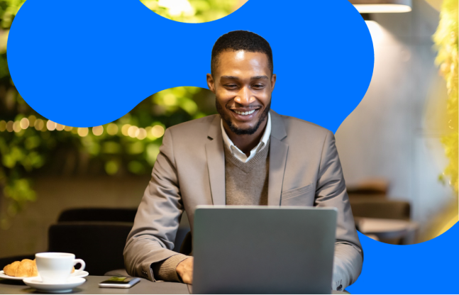 Smiling product tech professional working on a laptop at a café table with coffee and phone nearby, set against a modern workspace backdrop
