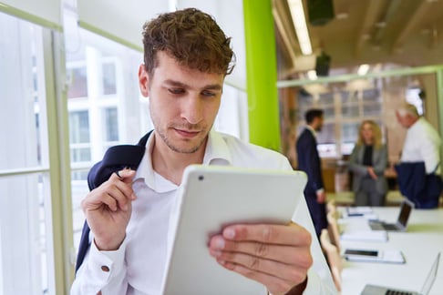 Professional reading data on a tablet while standing in an office.